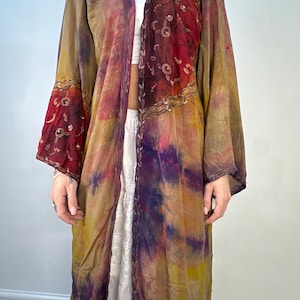 May include: A long, flowing tie-dye robe with a purple, yellow, and red color scheme. The robe has a hood and embroidered details on the sleeves and front.