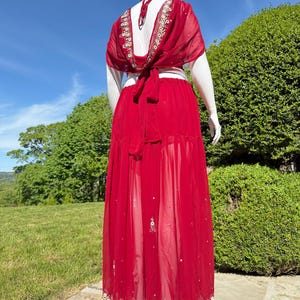 May include: A red, sheer maxi skirt with gold embroidery and a matching top. The top has a low back and ties at the waist.