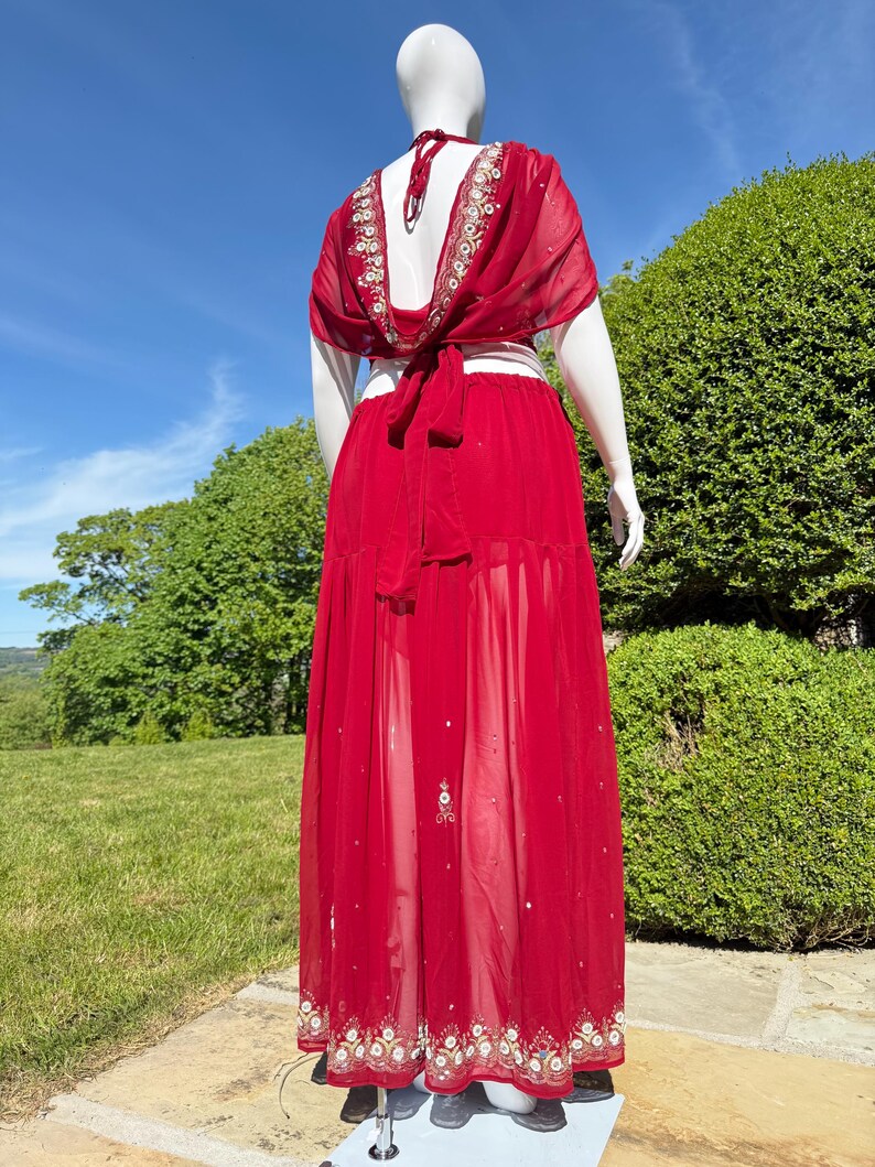 May include: A red, sheer maxi skirt with gold embroidery and a matching top. The top has a low back and ties at the waist.