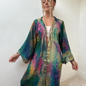 May include: A long, flowing robe with a vibrant, abstract pattern in shades of green, blue, pink, and yellow. The robe has long sleeves and a loose fit, suggesting a bohemian or artistic style. The fabric appears lightweight and flowing.