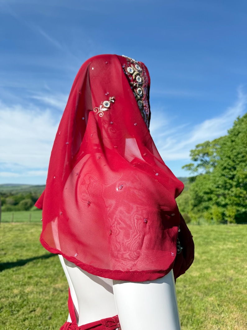 May include: A red sheer scarf with beaded embellishments. The scarf is draped over a white mannequin's head and shoulders.