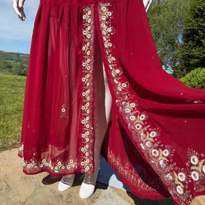 May include: A long red maxi dress with a front slit and intricate gold and silver embroidery along the hem.