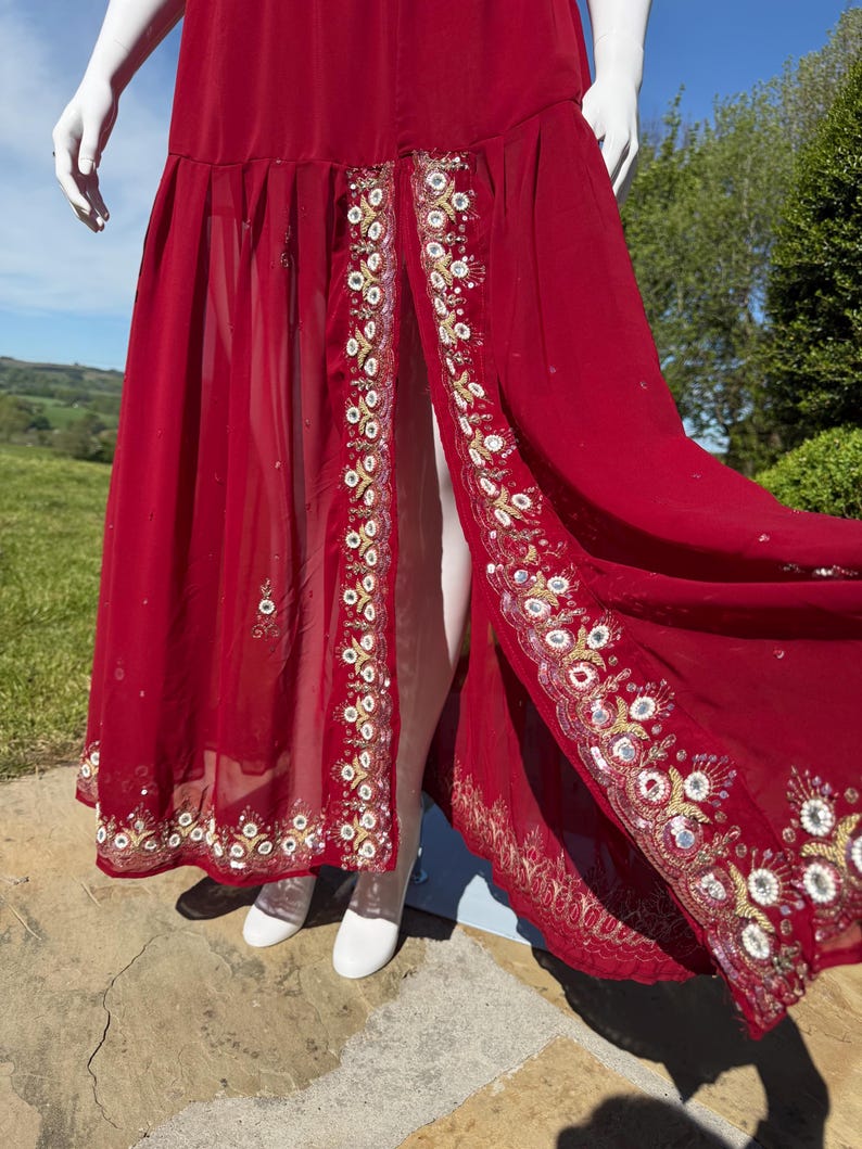 May include: A long red maxi dress with a front slit and intricate gold and silver embroidery along the hem.