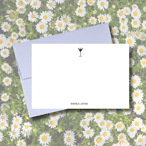 Può includere: Set di cancelleria bianco con illustrazione di bicchiere da cocktail e testo "BIANCA JAYDE". Il set include un biglietto vuoto e una busta abbinata, perfetto per note personali. Sfondo floreale.