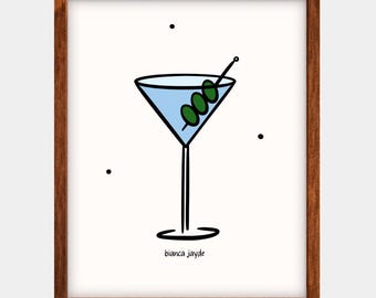 May include: A framed print with a minimalist illustration of a martini. The cocktail glass is filled with blue liquid and garnished with three green olives on a toothpick. The artwork includes the text "bianca jayde".
