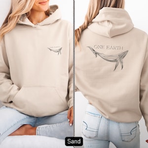 Könnte beinhalten: Sandfarbener Kapuzenpullover mit Fronttasche und Kapuze. Auf der Vorderseite befindet sich eine kleine Walgrafik mit dem Text "ONE EARTH". Auf der Rückseite des Hoodies ist eine größere Walgrafik und der Text "ONE EARTH" zu sehen.