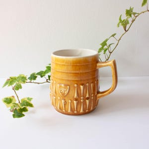 Peut inclure: Une chope à bière vintage en céramique avec une anse. La chope est de couleur ambre avec un intérieur blanc. Elle présente un motif décoratif de lignes verticales et un écusson avec les lettres "BP".