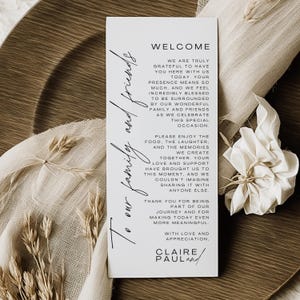 May include: A white welcome card with black script, featuring the text "Welcome" and a heartfelt message. The card is set against a neutral background with decorative elements, perfect for a wedding or special event.