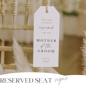 May include: A white reserved seat sign for the Mother of the Groom, hanging from a wooden chair. The sign includes the text "This seat is kindly reserved for the Mother of the Groom" and the names Sylvia Kerry.