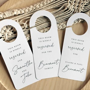 May include: Three white door hangers with the text "This room is kindly reserved" and personalised names. The first hanger says "Samantha and John", the second says "Beaumont Family", and the third says "Claire & Paul Beaumont".