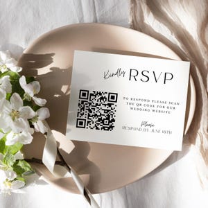 以下が含まれることがあります： 白いRSVPカードに黒いQRコードと「Kindly RSVP」と「返信するには、QRコードをスキャンして結婚式ウェブサイトをご覧ください。6月18日までに返信してください。」というテキストが書かれています。