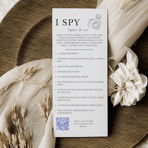 May include: A white card with the text "I Spy Capture the Love" and a list of things to find at a wedding. The card also includes a QR code with the text "Please scan this QR code and share your photos."