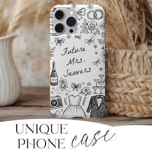 May include: A white phone case with a black and white sketch design. The case features drawings of bows, flowers, champagne, a camera, a wedding dress, a tuxedo, and the text "Future Mrs. Seavers."