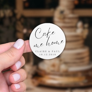 May include: White round sticker with black text that says "Cake me home" with the names Claire & Paul and the date 18.12.2018.