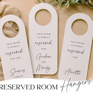 May include: Three white reserved room hangers with a rounded top and a hole for the door handle. Each hanger has the words "This room is kindly reserved for" printed in black, with a family name or couple's names below.