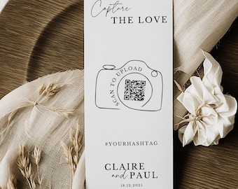 May include: A white wedding invitation card featuring the text "Capture the Love" and a camera graphic with a QR code. The card also includes the text "Scan to Upload", a hashtag, and the names "Claire and Paul" with the date 18.12.2025.