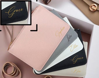 May include: Five personalized cosmetic bags in various colors with gold lettering. The bags are stacked on top of each other. The names on the bags are Grace, Sophia, Isla, Ella, and Mia.