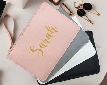 May include: A set of five zippered pouches in pink, gray, white, black, and beige. The pink pouch has the name "Sarah" written in gold lettering.