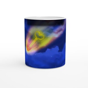 May include: White ceramic mug with a celestial design. A yellow heart-shaped key is set against a backdrop of a colourful, glowing comet streaking across a deep blue night sky with white clouds and stars. The mug has a glossy finish.
