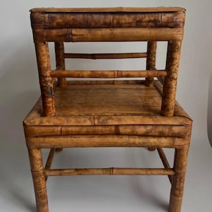 May include: Two-piece bamboo furniture set. The larger piece is a small chair or stool, and the smaller piece is a matching stool. Both pieces are constructed from natural bamboo poles, showcasing a warm, brown color with visible knots and textures.