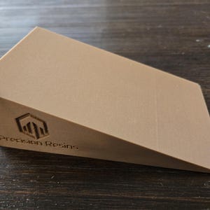 Puede incluir: Una cuña de forma triangular de color marrón claro con un logotipo que dice "Precision Resins" en la parte delantera.