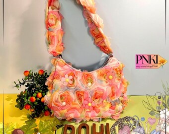 May include: A floral handbag with a ruffled strap and body. The bag is covered in fabric roses in shades of pink, peach, and yellow. Small white and yellow flowers are interspersed among the roses. The bag has a curved shape and a silver chain closure.