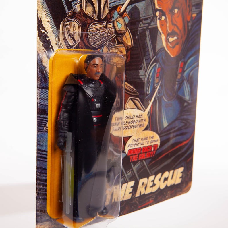 May include: A retro action figure of a character in a black outfit with a long coat, holding a green lightsaber. The figure is in a clear plastic package with a yellow backing card featuring comic book-style art and the text "THE RESCUE".