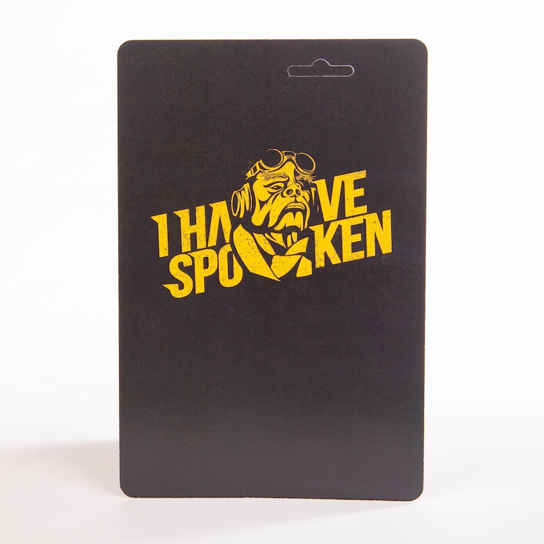 May include: Black rectangular card with a rounded top and a hole for hanging. The card features yellow text and a graphic of a man with goggles. The text reads "I HAVE SPOKEN".