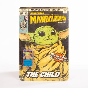 Puede incluir: Una portada de c&oacute;mic de Star Wars de estilo vintage con The Mandalorian y The Child. La portada muestra una imagen grande de The Child, con una peque&ntilde;a figura de acci&oacute;n de The Child en una cuna azul y roja. El c&oacute;mic est&aacute; etiquetado como "Cap&iacute;tulo 2".