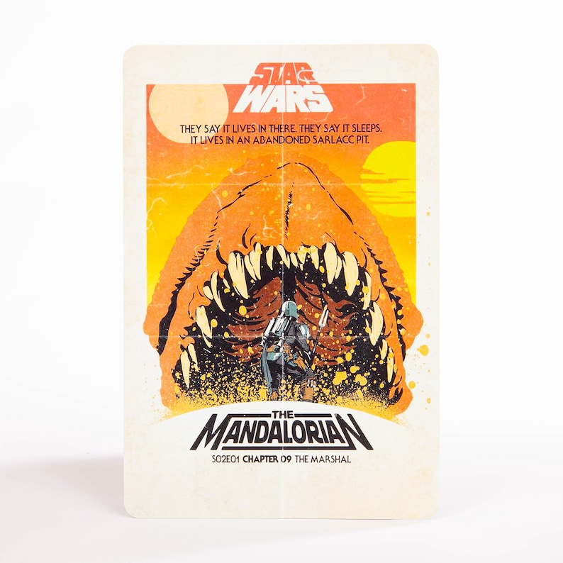 May include: A Star Wars trading card featuring a scene from The Mandalorian. The card has an orange and yellow background with the text "THEY SAY IT LIVES IN THERE. THEY SAY IT SLEEPS. IT LIVES IN AN ABANDONED SARLACC PIT." The Mandalorian is in the foreground.