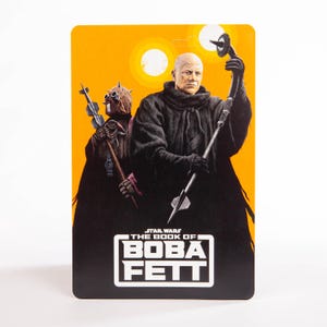 May include: A Star Wars: The Book of Boba Fett card featuring two figures in black cloaks against an orange background with two suns. The card has the show's logo in white.