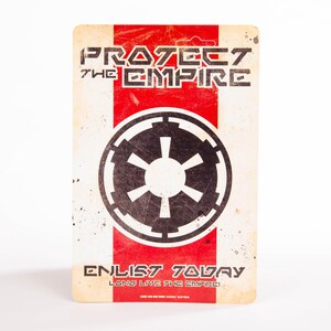 May include: A rectangular sign with a distressed, vintage aesthetic. The design features a red vertical stripe against a cream background. Bold text reads "PROTECT THE EMPIRE" and "ENLIST TODAY" with a black Imperial symbol.