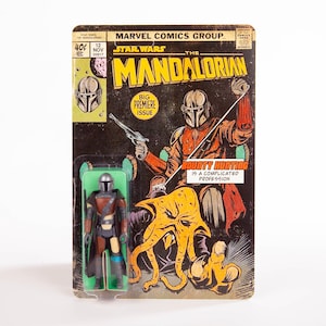 May include: A vintage Star Wars: The Mandalorian action figure on its original comic book-style packaging. The packaging features a comic book cover with the Mandalorian and the text "BIG PREMIERE ISSUE". The figure is in a green plastic blister pack.