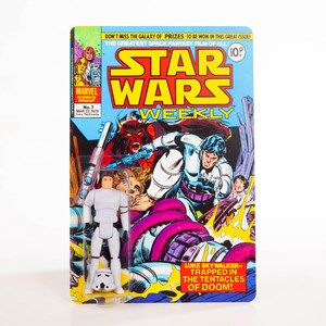 Może przedstawiać: Komiks Star Wars Weekly w stylu vintage z figurką Luke'a Skywalkera. Komiks zawiera żywe ilustracje i tekst "STAR WARS WEEKLY" dużymi żółtymi literami. Figurka jest biała i zawiera hełm szturmowca.