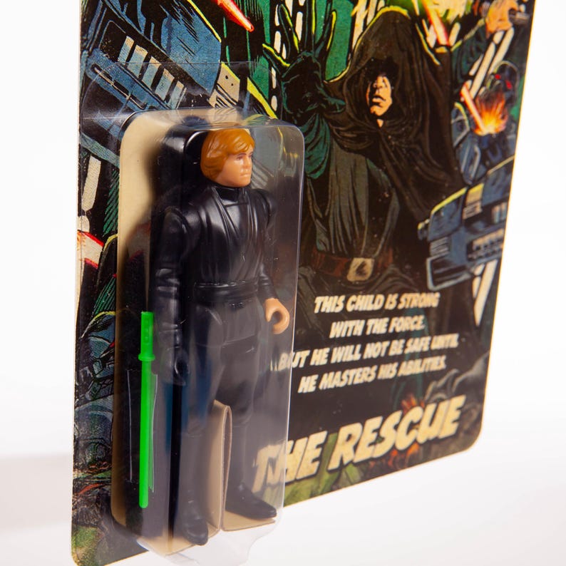 May include: Vintage action figure of a character in a black outfit with a green lightsaber, packaged on a card with illustrations and text that reads "THE RESCUE". The figure is in a clear plastic bubble.