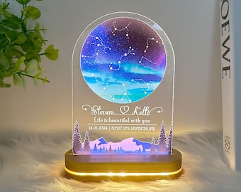 Puede incluir: Una luz nocturna personalizada con una base de madera y un panel de acrílico transparente que presenta un diseño de constelación, los nombres de una pareja, "Steven & Kelli", el texto "Life is beautiful with you" y la fecha y las coordenadas "14.01.2024 | 30°20'12'S 180°05'30.6°E".