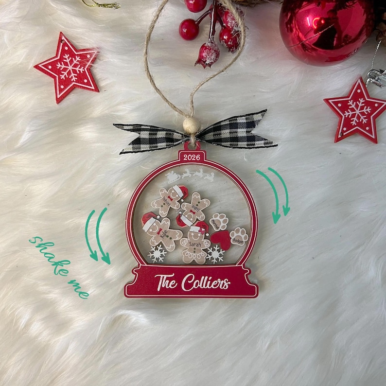 May include: A globe-shaped Christmas ornament with a red frame, featuring the text 2026 and The Colliers. Inside are loose wooden gingerbread figures, paw prints, and hearts. It includes a black and white checkered bow and a jute twine hanger.
