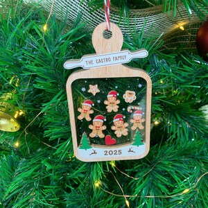 May include: Wooden Christmas ornament with a rolling pin design, featuring the text "THE CASTRO FAMILY." Inside the ornament is a festive scene with gingerbread people, stars, trees, and the year "2025."