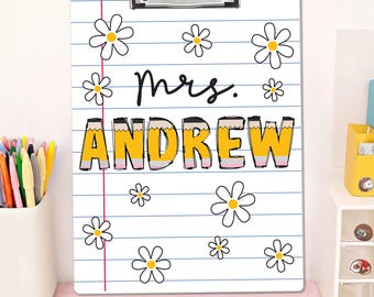 May include: A white clipboard with a floral design and the name "Mrs. Andrew" in a pencil-themed font. The clipboard features a metal clip at the top and is decorated with daisies and blue lined paper.