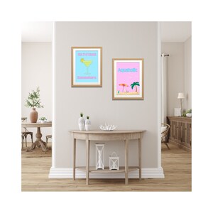 May include: Two framed art prints with a beach theme. One print features a cocktail and the text "It's 5 o'clock Somewhere" on a light blue background. The other print shows a beach scene with the word "Aquaholic" on a pink background.