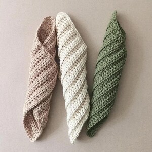 May include: Three handmade crochet spiral-shaped washcloths in a neutral palette. The washcloths are in shades of beige, cream, and olive green. The crochet stitch creates a textured, twisted design. These cloths are ideal for kitchen or bathroom use.