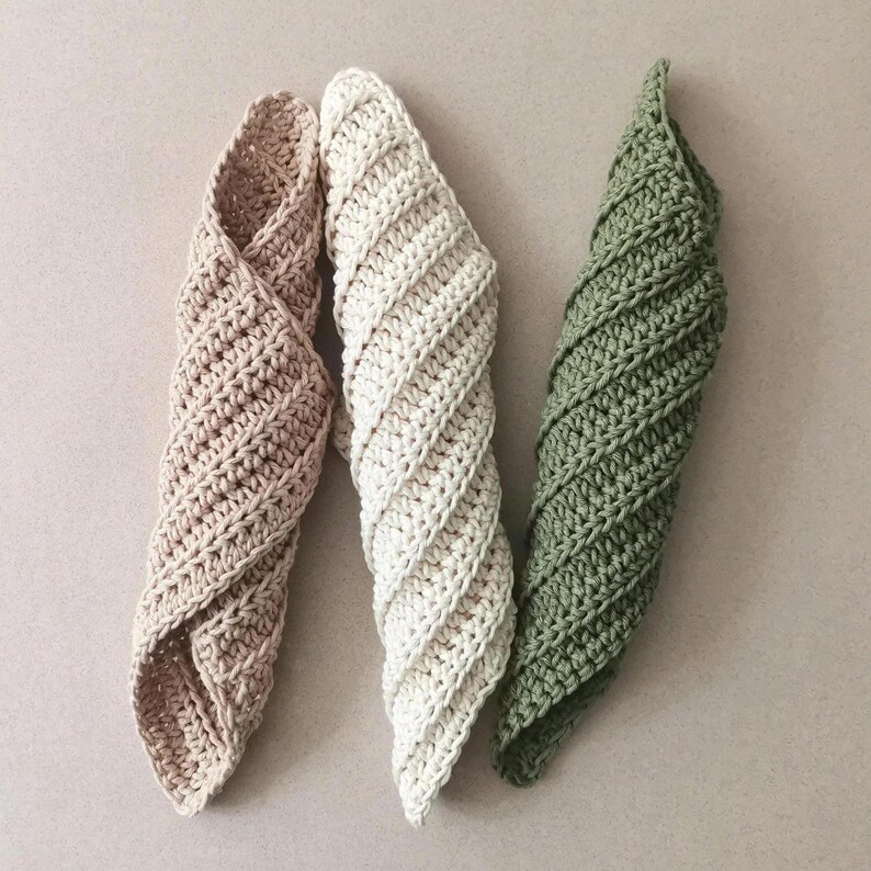 May include: Three handmade crochet spiral-shaped washcloths in a neutral palette. The washcloths are in shades of beige, cream, and olive green. The crochet stitch creates a textured, twisted design. These cloths are ideal for kitchen or bathroom use.