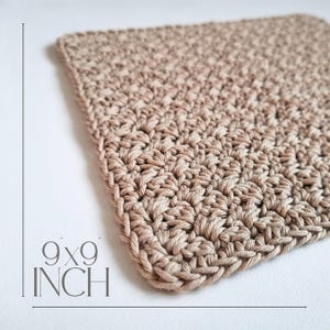 May include: A square, beige crochet item, measuring 9x9 inches. The handmade piece features a textured stitch pattern and a defined border. The neutral color and simple design suggest a versatile home decor item, such as a washcloth or coaster.