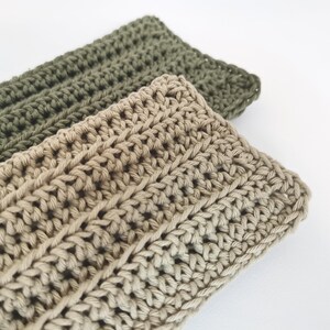 May include: Two handmade crochet headbands. One is a light tan color, and the other is olive green. The headbands are made with a thick yarn and have a ribbed texture. The headbands are displayed on a white background.