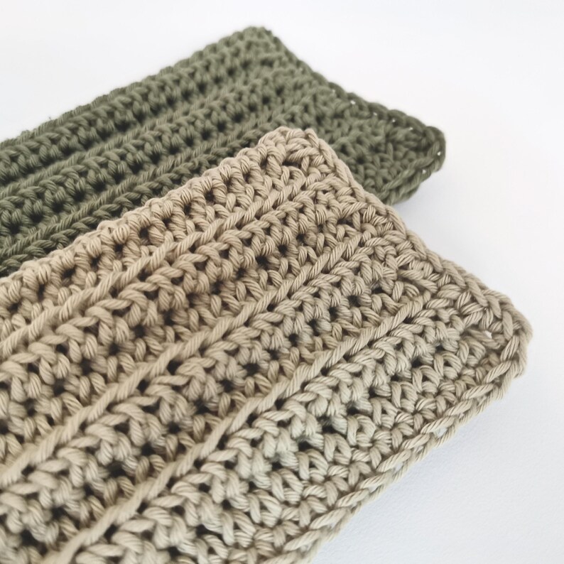 May include: Two handmade crochet headbands. One is a light tan color, and the other is olive green. The headbands are made with a thick yarn and have a ribbed texture. The headbands are displayed on a white background.