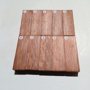 Puede incluir: Diez bloques de madera rectangulares dispuestos en dos filas. Los bloques son de color marrón rojizo con veta de madera visible. Cada bloque está numerado con un número blanco del 1 al 10.