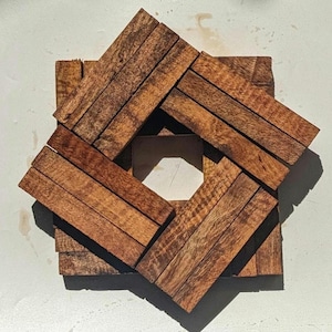 Puede incluir: Un objeto de madera en forma de estrella hecho de múltiples tiras de madera marrón, dispuestas en un patrón geométrico, creando una abertura cuadrada en el centro.
