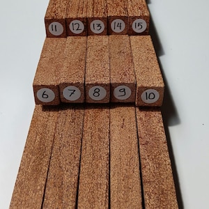 May include: A collection of rectangular wooden blocks with a textured, brown surface. Each block is labeled with a number from 1 to 20. The blocks are arranged in a stacked formation, showcasing their varying lengths and widths.