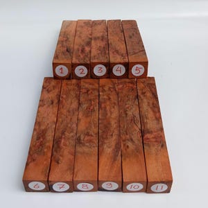 Può includere: Undici blocchi di legno rettangolari con un motivo a venature di radica marrone rossiccio. Cinque blocchi sono impilati sopra altri sei. Ogni blocco ha un adesivo bianco con un numero da 1 a 11.