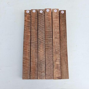 May include: Six rectangular wooden planks with a reddish-brown hue and a prominent wood grain pattern. Each plank is labeled with a number from one to six on a small white sticker. The planks are arranged side by side.